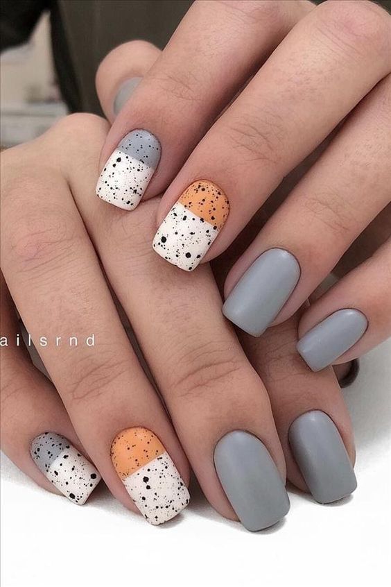 Neutral manicure with grey, tan, white, and splattered black design.